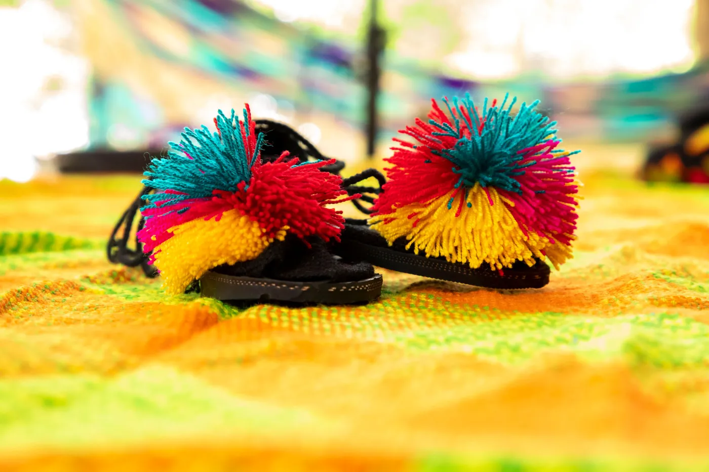 Sandalias con pompones de colores sobre una tela tejida amarilla.
