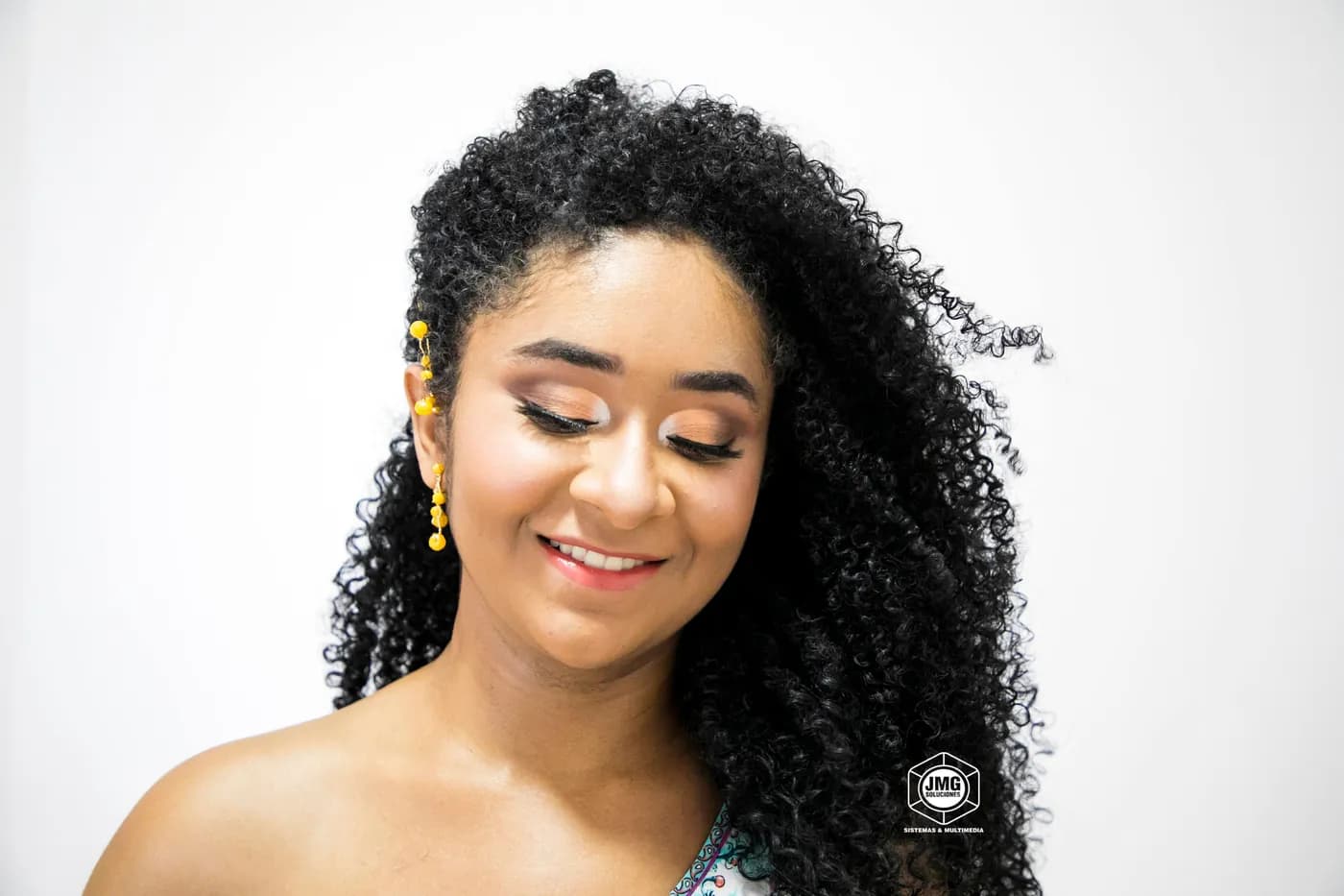 Retrato de estudio de una mujer sonriente de cabello rizado sobre fondo blanco.