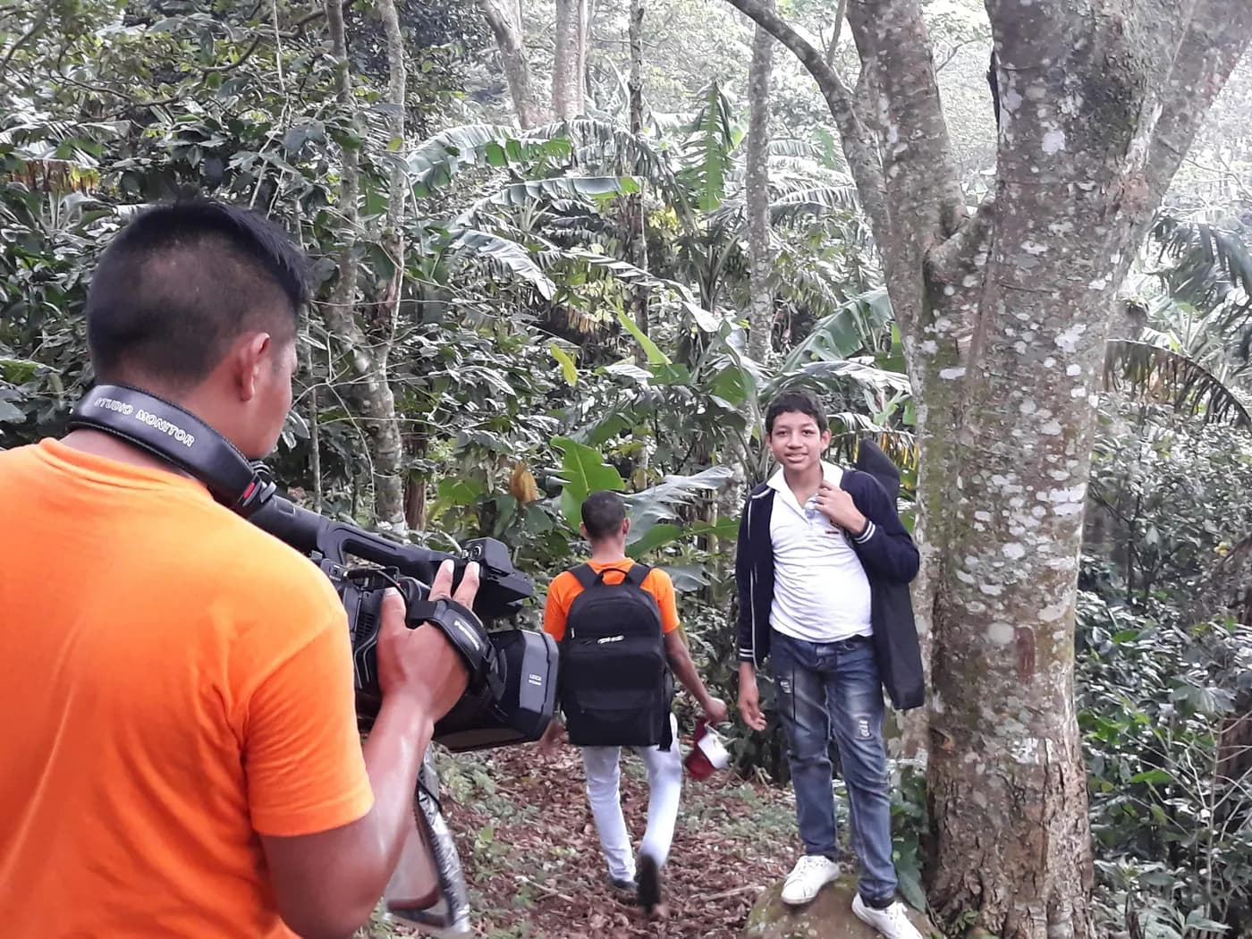 Camarógrafo de JMG con camiseta naranja graba a un grupo que camina por un sendero en el bosque.