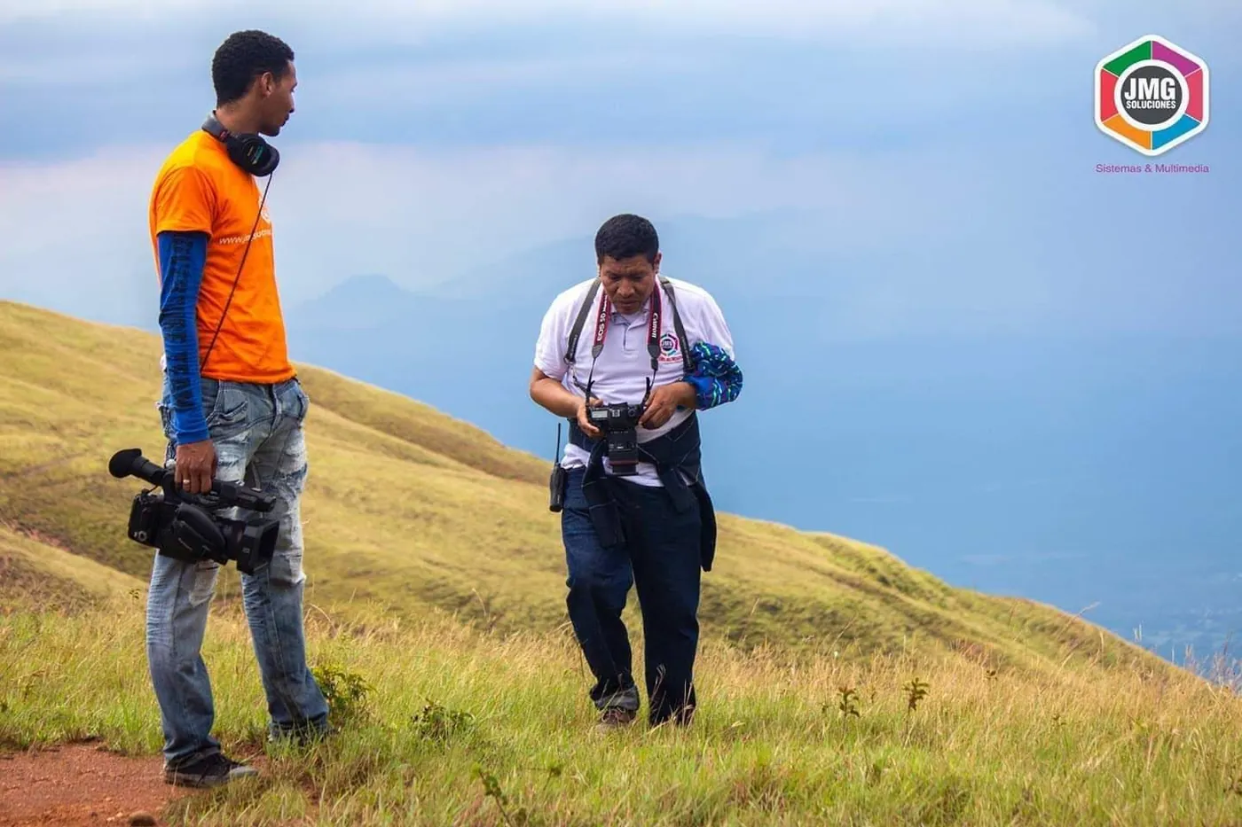 Dos integrantes de JMG con cámara de video y cámara fotográfica preparan una toma en la ladera de una montaña.