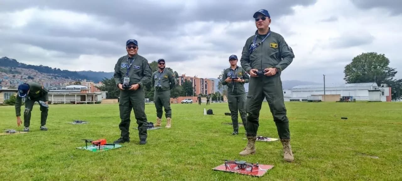 Pilotos con overol de vuelo y control en mano practican el despegue de drones en un campo abierto.