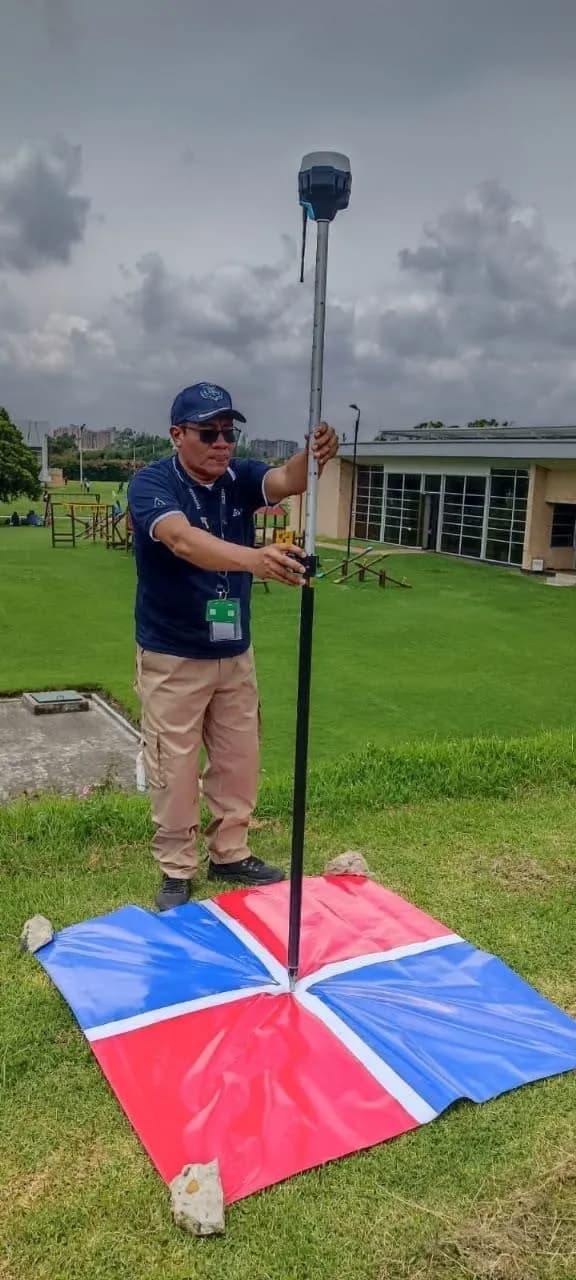 Integrante de JMG ubica un receptor GNSS sobre un punto de control en tierra, marcado con una lona roja y azul.