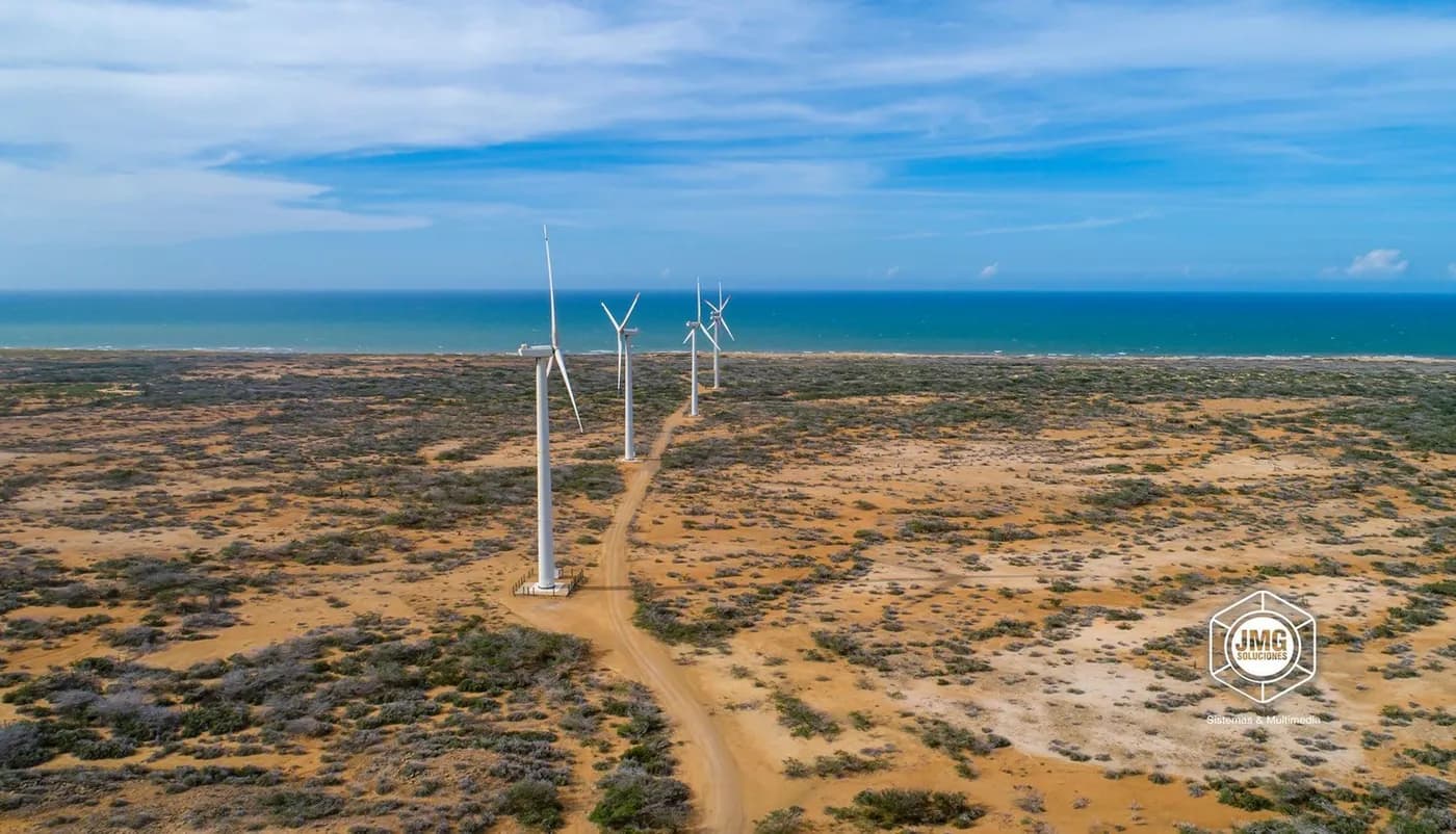 Vista aérea con dron de aerogeneradores en el desierto, con el mar al fondo.