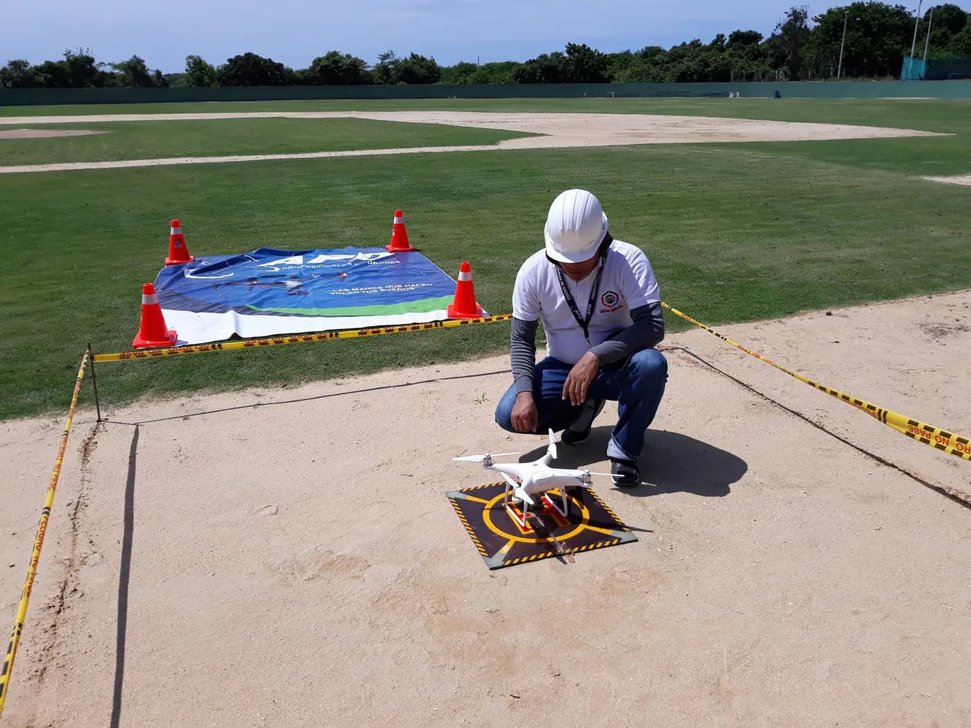 Piloto de JMG con casco blanco prepara el despegue de un dron desde una plataforma, en una zona delimitada con cinta y conos.