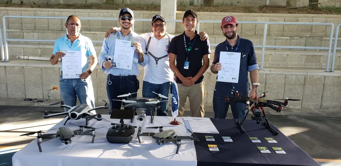 Pilotos muestran sus certificados junto a una mesa con drones y controles, al cierre de un curso de formación.