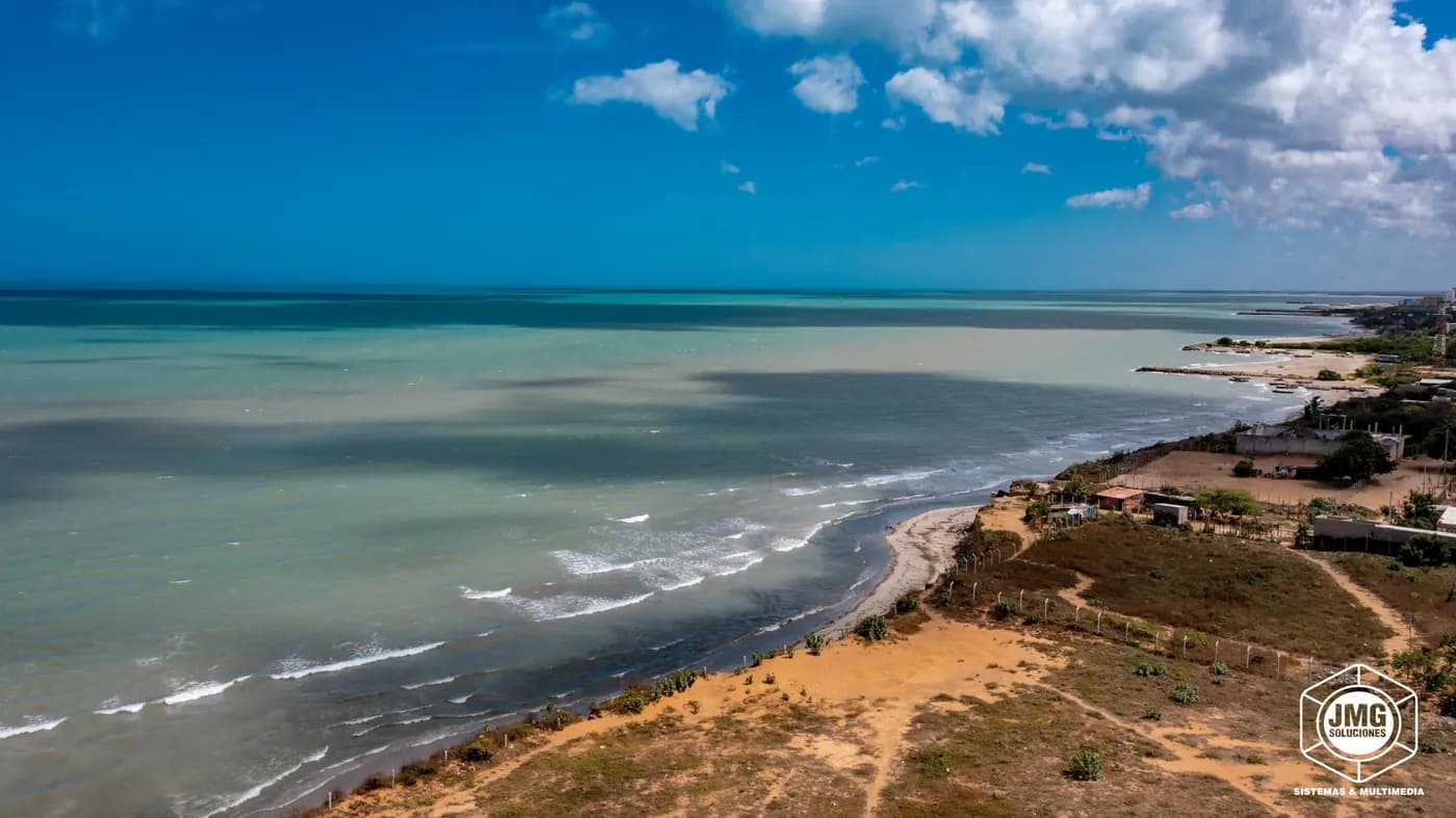 Vista aérea con dron de la costa, con el oleaje rompiendo sobre la playa y el mar en tonos verdes.