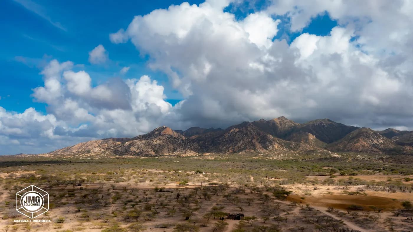 Vista aérea con dron de un paisaje desértico con una serranía al fondo bajo grandes nubes.
