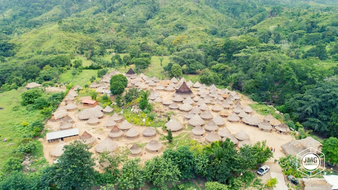 Vista aérea con dron de un caserío de techos de palma en medio de montañas cubiertas de bosque.