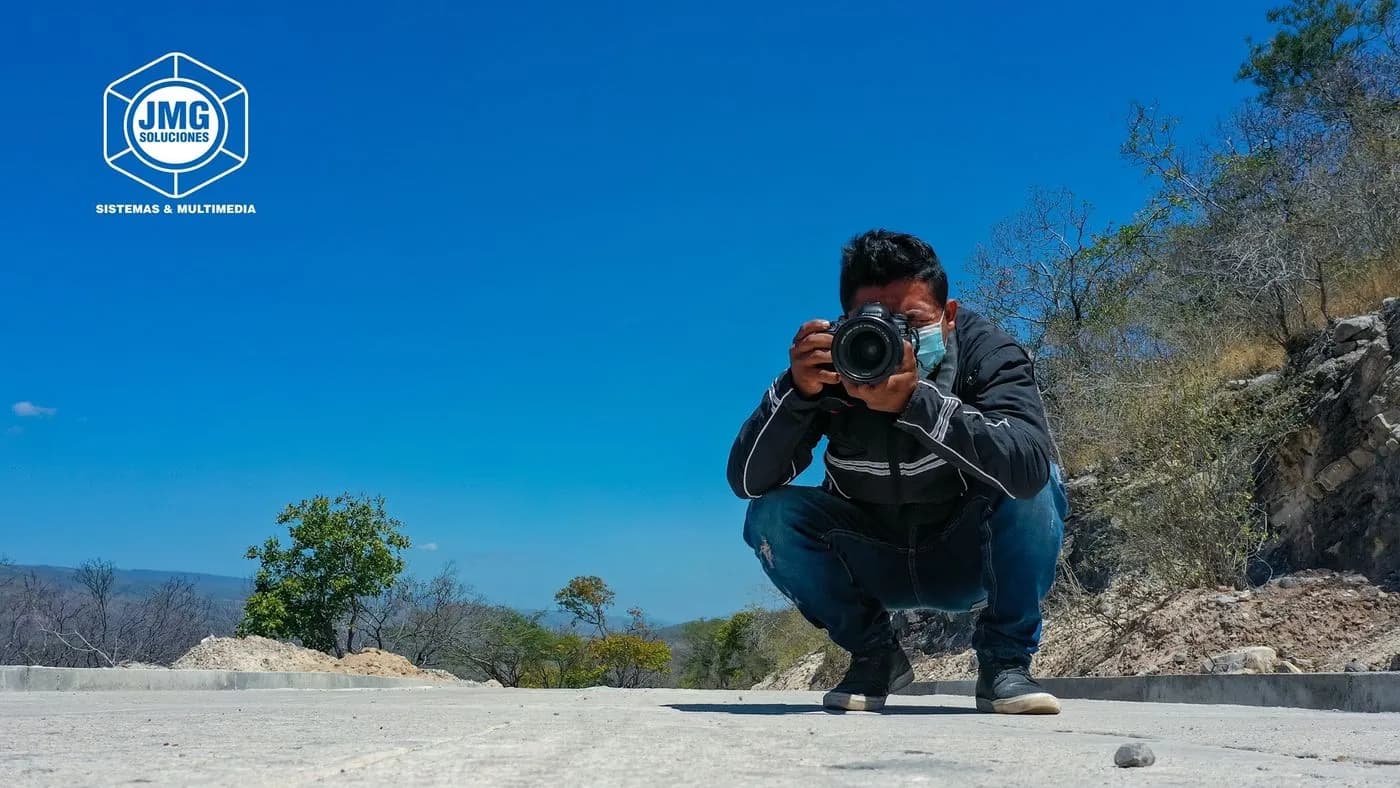 Fotógrafo de JMG en cuclillas sobre una vía de concreto dispara su cámara bajo un cielo despejado.
