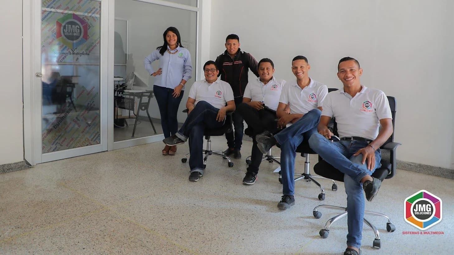 Equipo de JMG reunido en la oficina junto a la puerta con identidad corporativa.