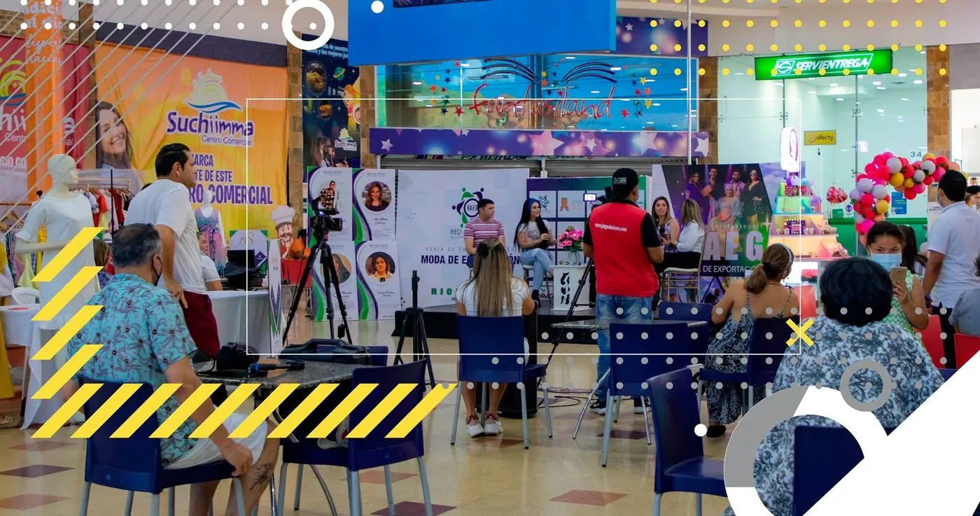 Equipo de JMG transmite una feria de emprendedores en un centro comercial, con cámara sobre trípode ante el escenario.