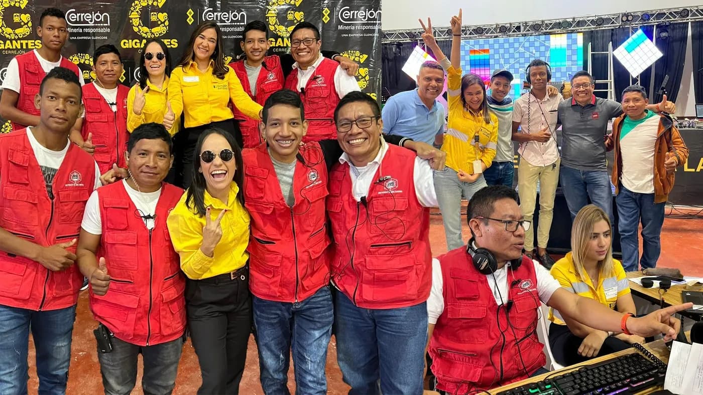 Equipo de JMG y del programa «Gigantes» de Cerrejón celebran frente al fondo de prensa, mientras un operador de JMG trabaja en el control de la transmisión.