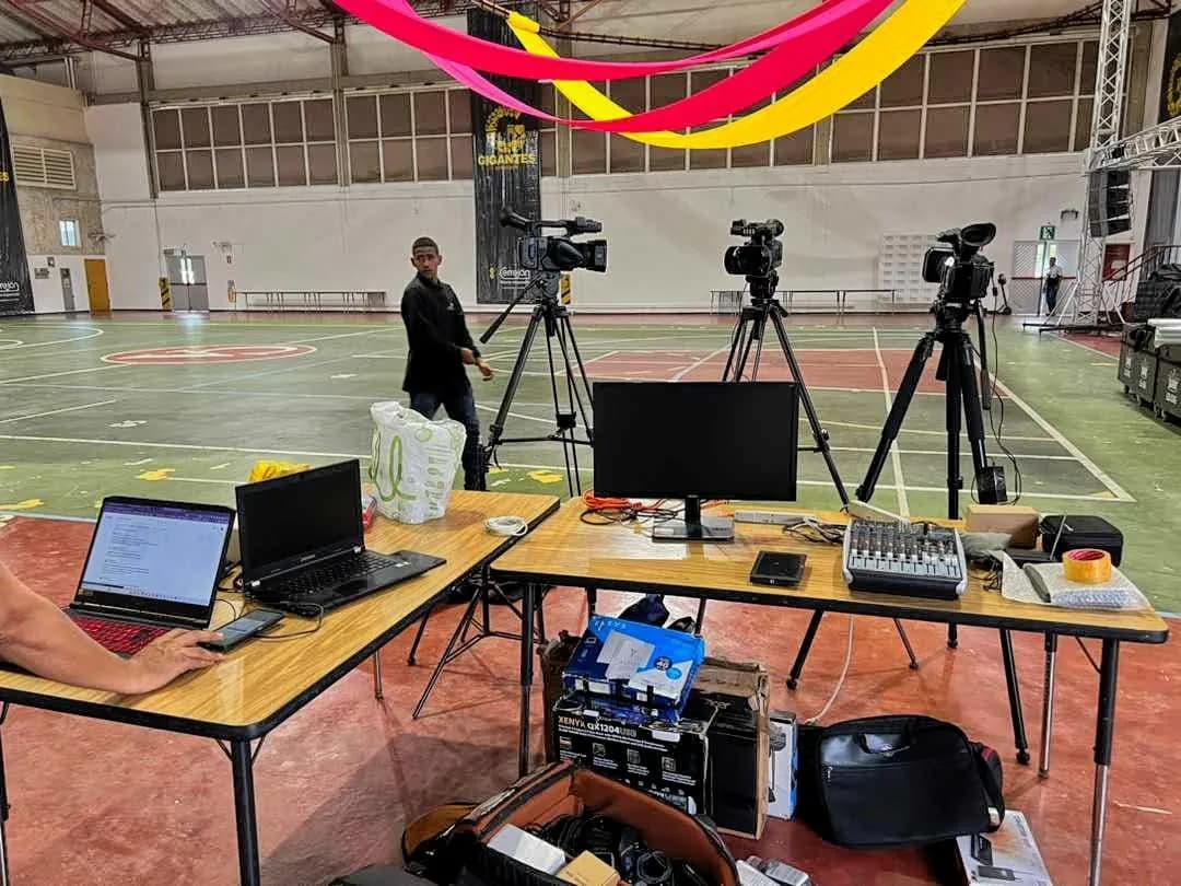 Montaje de JMG en un coliseo: cámaras sobre trípodes, monitor, computadores y consola listos para transmitir.