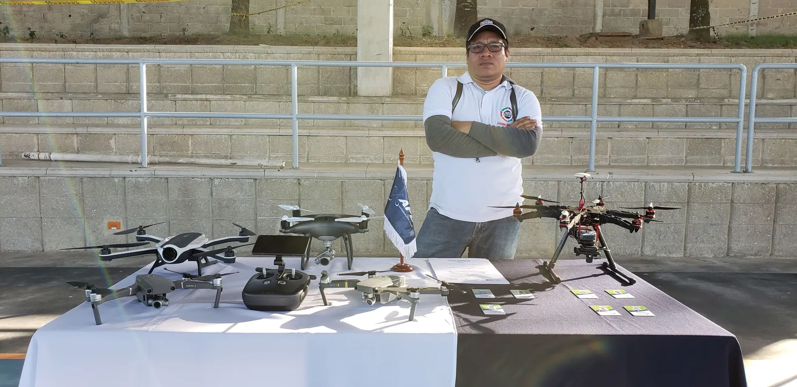 Jaider Mengual con los brazos cruzados detrás de una mesa con drones y equipos de vuelo.